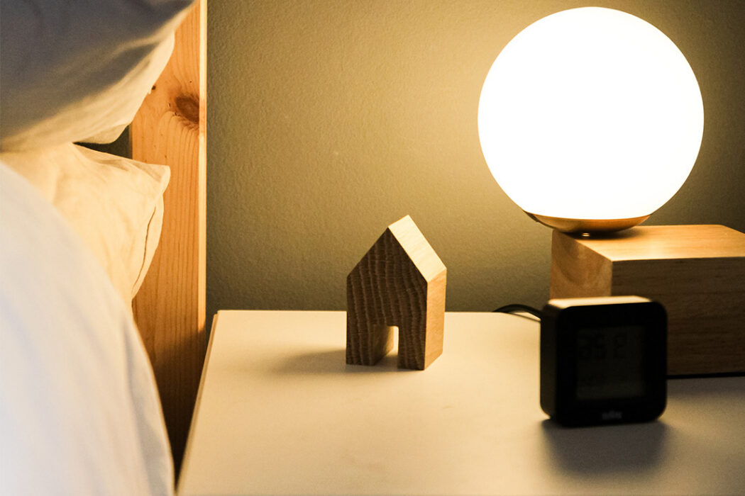Ett nattduksbord med lampa och ett litet hus i trä