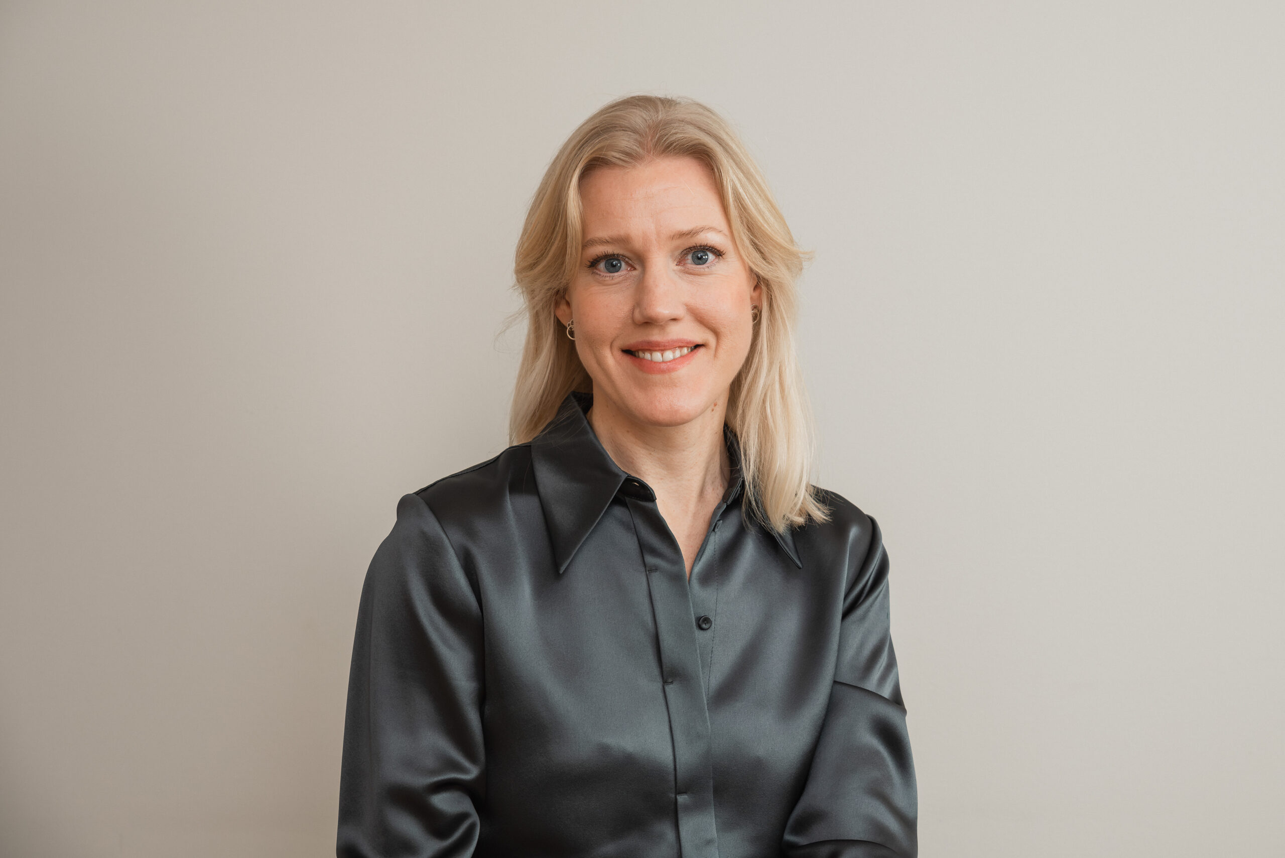 Person med blont hår och grå skjorta sitter mot en ljus bakgrund.
