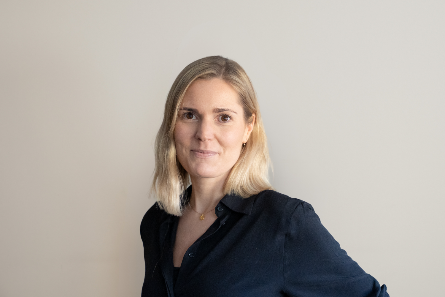 En person med axellångt blont hår och mörkblå skjorta står med sidan mot kameran.